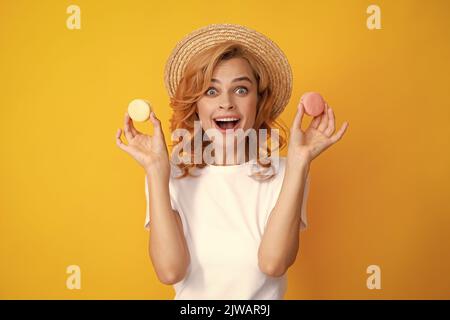 Une jeune femme adorable tient un macaron. Belle jeune fille souriante mangeant des macarons colorés sur fond jaune. Banque D'Images