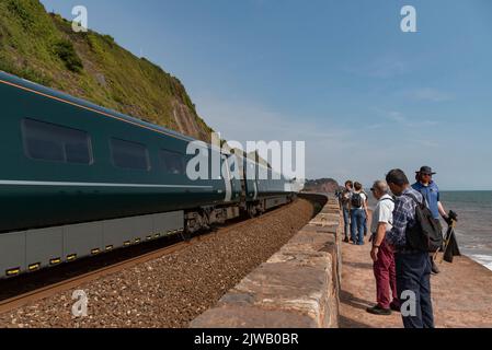 Teignmouth, Devon, Angleterre, Royaume-Uni. 2022. Les vacanciers s'arrêtent au bord de la voie pour voir un train de voyageurs se diriger vers Teignmouth sur la côte sud-ouest. Banque D'Images