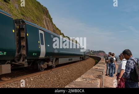 Teignmouth, Devon, Angleterre, Royaume-Uni. 2022. Les vacanciers s'arrêtent au bord de la voie pour voir un train de voyageurs se diriger vers Teignmouth sur la côte sud-ouest. Banque D'Images