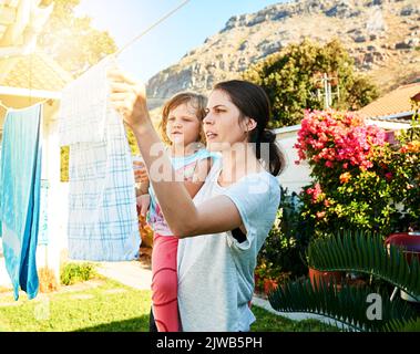 Apprendre à connaître le travail des mamans. Une mère et une fille qui pendent le linge ensemble à l'extérieur. Banque D'Images