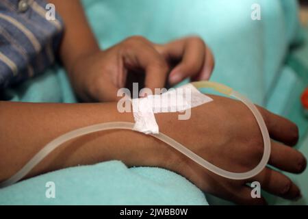 Patiente avec iv à portée de main pour fixer le pansement à l'hôpital. Main d'une patiente asiatique avec un tube d'écoulement intraveineux dans un lit d'hôpital. Banque D'Images