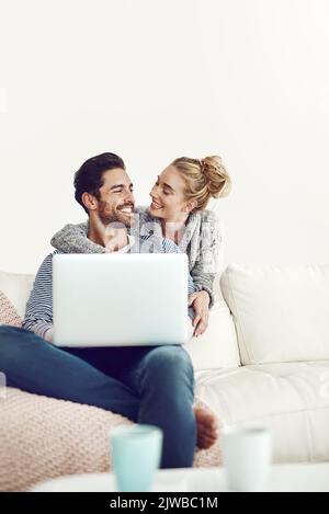 Un jeune couple qui utilise un ordinateur portable sur son canapé à la maison, se connecte avec ses amis et sa famille. Banque D'Images