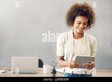 Le succès vient de ceux qui travaillent pour elle. Une jeune femme d'affaires attirante travaillant sur sa tablette à la maison. Banque D'Images