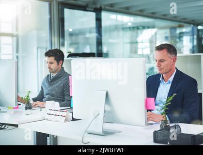 Travailler individuellement pour la réussite collective : deux hommes d'affaires travaillant à leur bureau. Banque D'Images