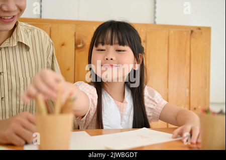 Adorable jeune fille asiatique aime dessiner et colorer sur un papier avec son professeur d'art en classe. Enfants concept d'activité Banque D'Images