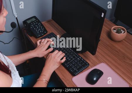 Femme travaillant à un bureau dans un bureau avec un ordinateur. Femme aux cheveux rouges travaillant comme agent de voyage sur l'ordinateur. Photo de haute qualité Banque D'Images