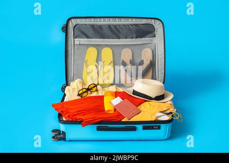 Valise avec vêtements, passeport, billet et accessoires de plage sur fond de couleur Banque D'Images