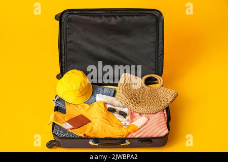 Valise avec vêtements, accessoires de plage, billet et passeport sur fond jaune Banque D'Images