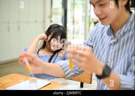 Adorable et adorable jeune fille asiatique couvrant ses oreilles tandis que son professeur fait une expérience chimique passionnante dans le laboratoire. Banque D'Images