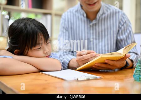 Une petite fille asiatique endormie penchée sur la table pendant que son professeur de mathématiques privé enseigne et montre la réponse sur le livre. Enfants et tutrice privée conce Banque D'Images