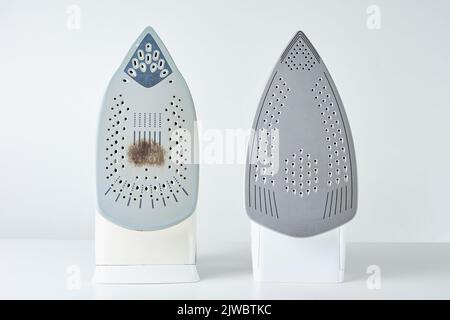 Fer ancien avec semelle endommagée et nouveau fer moderne sur fond blanc, entretien et entretien des appareils ménagers modernes Banque D'Images