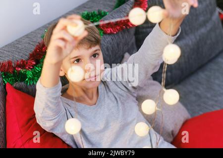 Portrait d'un garçon de Noël. L'enfant prépare des lumières de Noël pour décorer la maison. Banque D'Images