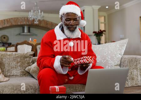 Homme afro-américain senior portant un costume du père noël et tenant des cadeaux Banque D'Images