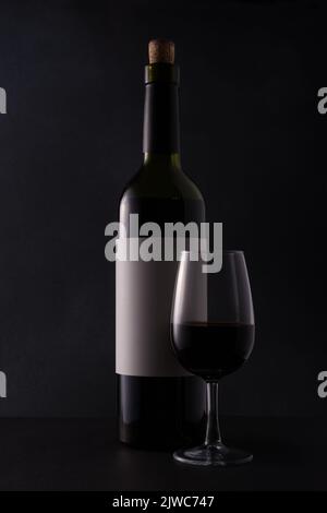 Bouteille de vin rouge avec modèle blanc ou étiquette maquette et verre sur fond noir Banque D'Images