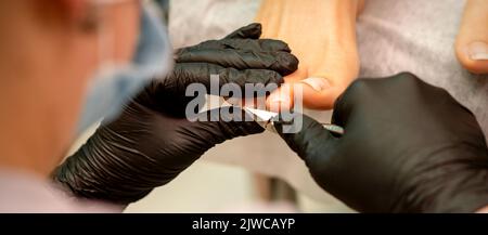 Pédicure professionnelle. Pédicure maître portant des gants en latex coupe les ongles du pied féminin dans le salon de beauté, gros plan Banque D'Images