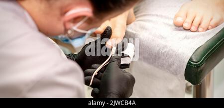 Pédicure professionnelle. Pédicure maître portant des gants en latex coupe les ongles du pied féminin dans le salon de beauté, gros plan Banque D'Images