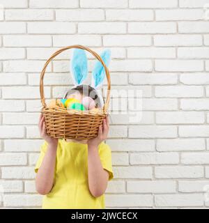 Garçon aux oreilles de lapin de Pâques avec panier en osier et œufs colorés. Copier l'espace Banque D'Images