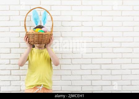 Garçon aux oreilles de lapin de Pâques avec panier en osier et œufs colorés. Copier l'espace Banque D'Images