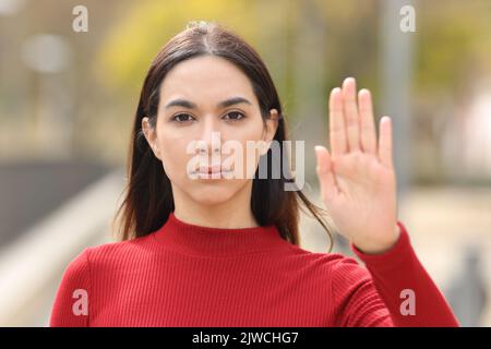 Vue de face portrait d'une femme sérieuse en rouge gestuelle arrêt avec la main dans la rue Banque D'Images