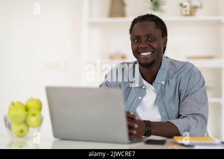 Concept freelance. Happy Young Black Man assis au bureau avec ordinateur portable Banque D'Images