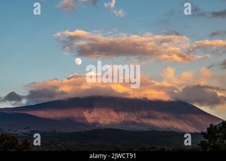 Une pleine lune s'élevant au-dessus de l'Etna, vue au coucher du soleil depuis le côté ouest du volcan Banque D'Images