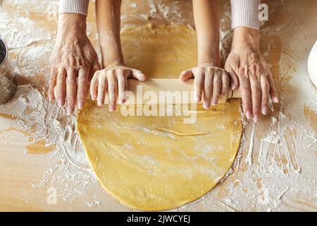 Les mains d'une petite fille européenne et d'une grand-mère âgée font de la pâte avec un rouleau pour pizza et biscuits Banque D'Images