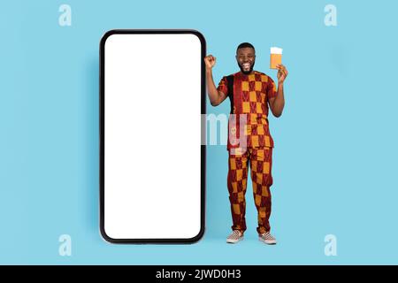 Black Man excitée avec Pasport et des billets debout près de l'immense smartphone blanc Banque D'Images