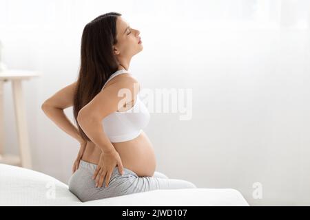 Femme enceinte souffrant de douleurs dorsales, assise sur le lit Banque D'Images