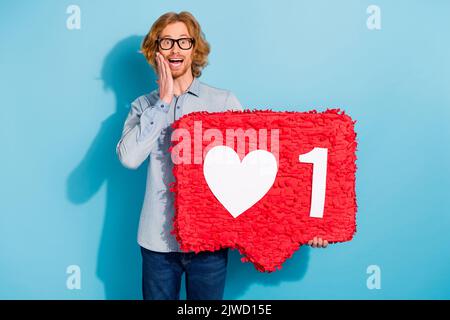 Photo de l'homme doux impressionné porter des lunettes de chemise en denim tenant le signe de rétroaction isolé couleur bleu arrière-plan Banque D'Images