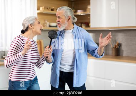 Couple senior positif s'amusant dans la cuisine intérieure, chantant et dansant Banque D'Images