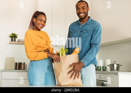 Souriants conjoints noirs déballant sac en papier avec des légumes et des fruits biologiques frais après l'épicerie Banque D'Images