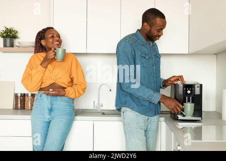 Un heureux couple afro-américain prépare un café frais aromatique avec une machine dans la cuisine, en savourant une boisson chaude le matin Banque D'Images