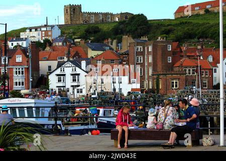 Fish and chips at the Seaside - les vacanciers apprécient leurs Fish & chips sur le côté ouest de la rivière Esk dans le Whitby Yorkshire. Derrière les bateaux dans le port peut être vu les bâtiments du côté est et au-dessus d'eux l'église paroissiale de Sainte Marie. Banque D'Images