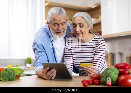 Conjoints aînés souriants effectuant des paiements en ligne avec une tablette numérique et une carte de crédit Banque D'Images