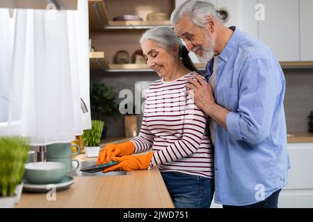 Portrait des conjoints aînés heureux laver les plats dans la cuisine après le déjeuner Banque D'Images