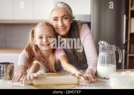 Bonne femme à la retraite dans le tablier enseignement petite fille faisant de la pâte en utilisant la goupille de fabrication des biscuits Banque D'Images