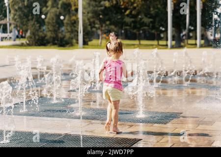 petite fille jouant avec de petites fontaines sur la place urbaine Banque D'Images