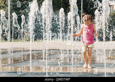 petite fille jouant avec de petites fontaines sur la place urbaine Banque D'Images