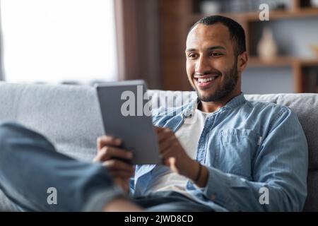 Un homme noir souriant se détendant avec une tablette numérique à la maison Banque D'Images