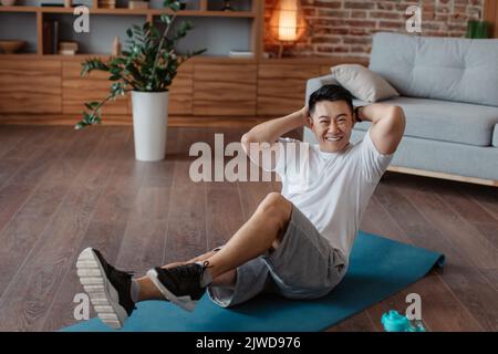 Homme asiatique heureux faisant des exercices d'abs, s'entraîner à la maison sur tapis de fitness, portrait en longueur Banque D'Images