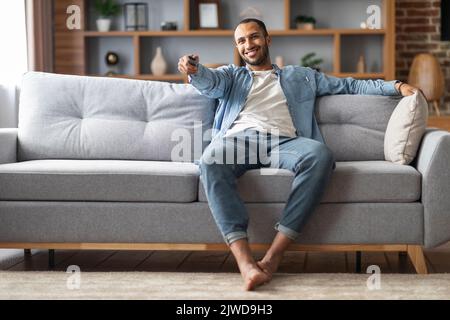 Détente à la maison. Beau Black Man assis sur un canapé et changer de chaîne de télévision Banque D'Images