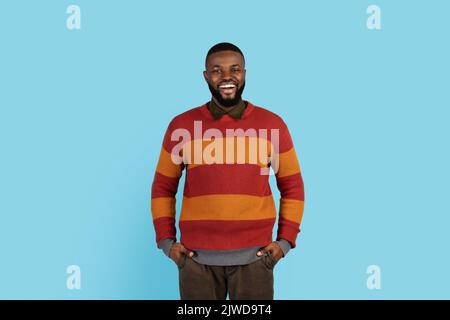 Homme noir positif debout avec les mains dans les poches et souriant à l'appareil photo Banque D'Images