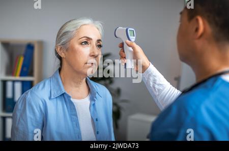 Adulte asiatique homme médecin vérifiant la température avec le thermomètre sans contact pour triste patient senior Banque D'Images