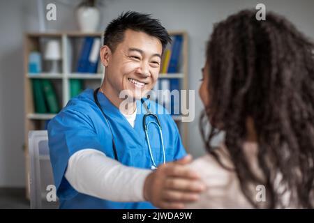 Le médecin chinois souriant adulte calme et soutient la jeune femme afro-américaine patiente en clinique Banque D'Images