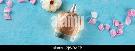 Panorama parfum rose. Bouteille de parfum floral, plan de pose à plat avec fleurs et pétales sur fond bleu, une bannière panoramique Banque D'Images