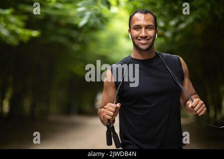 Sportif noir positif s'exerçant avec corde à sauter dans le parc public Banque D'Images