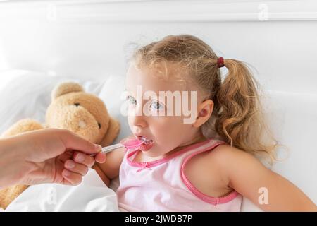 L'enfant boit du sirop à l'aide d'une cuillère de mesure. Banque D'Images