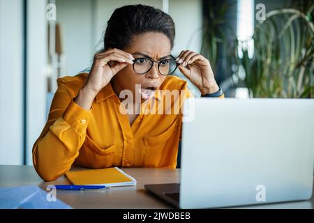 Femme d'affaires noire choquée regardant l'écran d'ordinateur portable avec la bouche ouverte, lisant des nouvelles choquantes d'affaires Banque D'Images