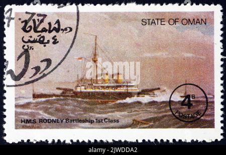 OMAN - VERS 1977: Un timbre imprimé dans l'État d'Oman montre le HMS Rodney, était l'un des deux navires de guerre de classe Nelson construits pour la Marine royale au milieu de 1920 Banque D'Images