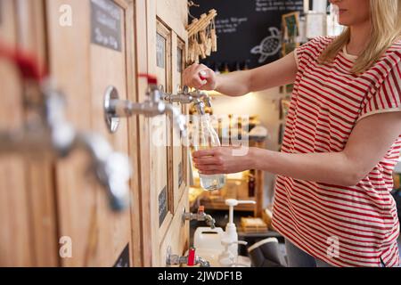 Gros plan de la femme qui recharge une bouteille de verre avec un nettoyant liquide dans un magasin sans plastique durable zéro déchet Banque D'Images